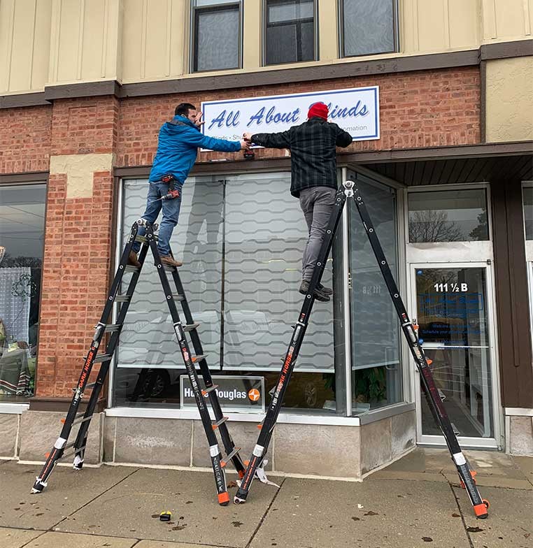 Two men on ladders putting up a sign on the business exterior